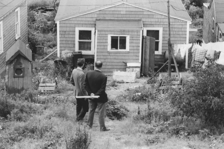 White city officials with a rolled up paper plan looking at a house ("Gone But Never Forgotten").